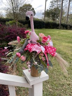 a pink flamingo stuffed animal sitting on top of a wooden bench next to flowers