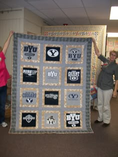 two women holding up a quilt with many logos on it