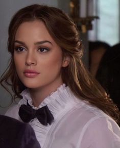 a woman with long hair wearing a white shirt and black bow tie looking at the camera