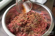 someone is adding seasoning to the ground beef in a large metal bowl on top of a counter