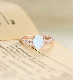 a white opal and diamond ring sitting on top of an open book