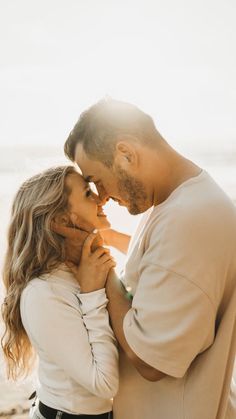 a man and woman standing next to each other on the beach with their arms around each other