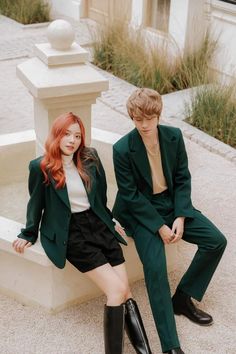 two people sitting next to each other in front of a fountain wearing green suits and black boots