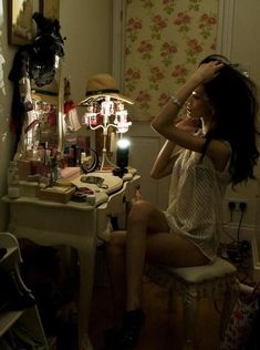 a woman sitting in front of a desk with a lamp on top of it next to a mirror