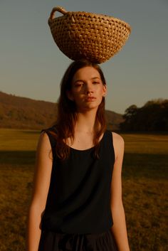 a woman standing in a field with a basket on top of her head, looking at the camera