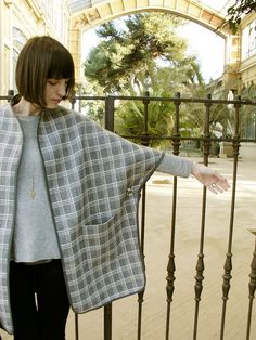 a woman standing next to a fence with her hand on the top of her jacket