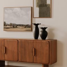 two black vases sitting on top of a wooden cabinet in front of a painting