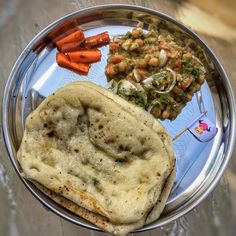 a metal plate topped with food on top of a wooden table next to carrots