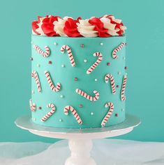 a blue cake decorated with candy canes and candies on a white pedestal against a teal background