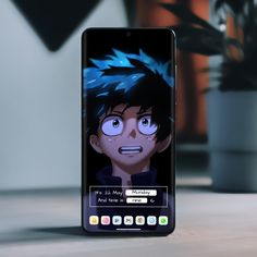 a cell phone with an anime character on the screen and a plant in the background