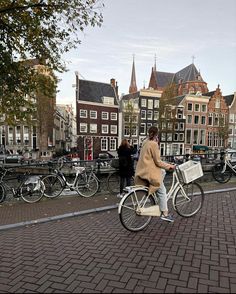 a woman riding a bike down a street next to tall buildings with bicycles parked on the sidewalk