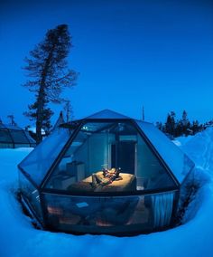 a glass house in the middle of snow covered ground with lights on it's windows