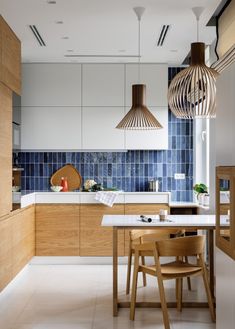 a kitchen with blue tiles and wooden furniture in the center, along with two pendant lights hanging from the ceiling