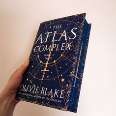 the atlas complex book is being held by a person's hand over a white wall