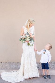 a young boy holding the hand of an older woman wearing a wedding dress and shoes