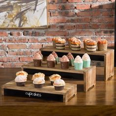 cupcakes are arranged on three tiered trays in front of a brick wall