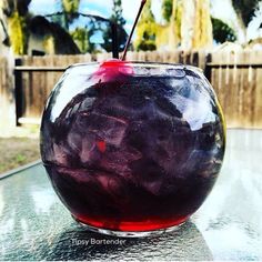 a glass filled with purple liquid sitting on top of a table next to a fence