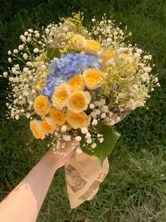 a bouquet of yellow and blue flowers is held by someone's hand in the grass