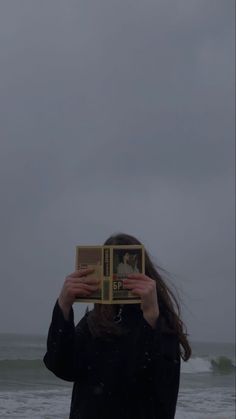 a woman is holding up a book in front of her face as she stands on the beach