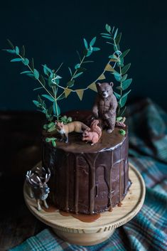 there is a chocolate cake decorated with animals and plants on top of the wooden stand