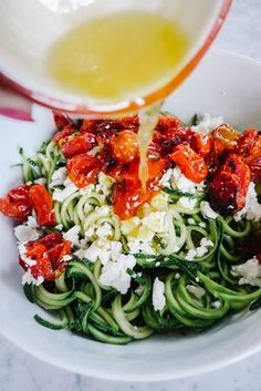 someone is pouring dressing over a bowl of green pasta with tomatoes and fettuccine