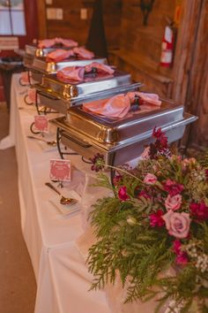 the buffet table is set up with silver trays and pink napkins on them