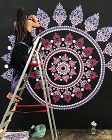 a woman on a ladder painting a wall with purple and white flowers in the center