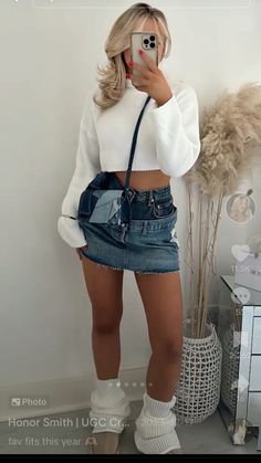 a woman taking a selfie while wearing a denim skirt and white top with high heels