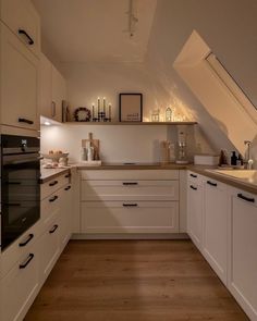 an attic kitchen with white cabinets and wood flooring is lit by recessed lighting