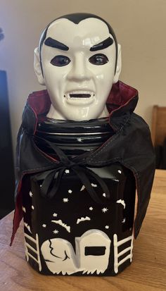 a white mask sitting on top of a wooden table next to a black box with red ribbon