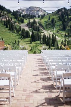 rows of white folding chairs set up for an outdoor wedding ceremony in the mountainside