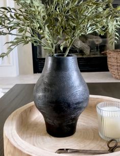 a black vase sitting on top of a wooden tray next to a candle and some scissors