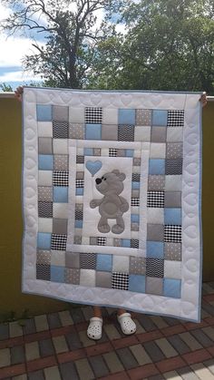 a person holding up a quilt with a teddy bear in the center and blue squares on it