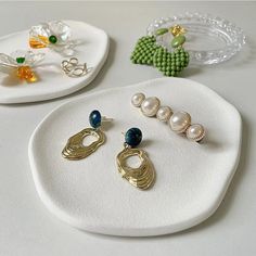 three pairs of earrings sitting on top of a white plate next to other jewelry pieces