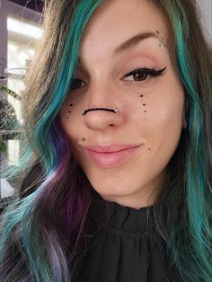 a woman with blue and green hair has black nose piercings