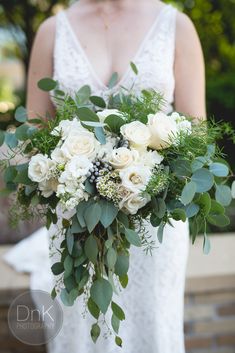 a bride holding a bouquet of white flowers and greenery