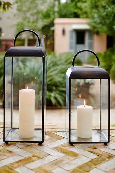 two lit candles sitting on top of a brick walkway