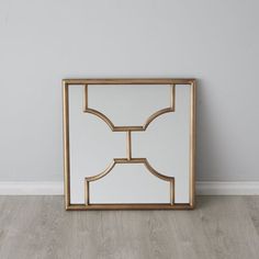 a mirror sitting on top of a wooden floor next to a white wall with a gold frame