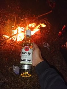 a bottle of bacardi sitting in front of a fire with someone holding it