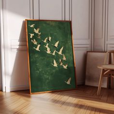 there is a painting on the floor with birds flying in the sky above it and a chair next to it