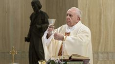 a priest holding a chalice in front of a statue