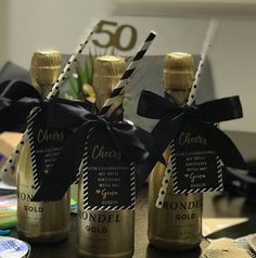 three bottles of wine with black and gold ribbons tied around them on a table next to other items