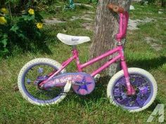 a pink bike with purple wheels is parked next to a tree in the grass and flowers