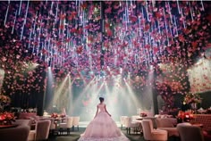 a woman in a wedding dress standing under a chandelier with flowers hanging from the ceiling