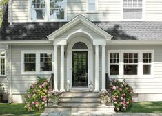 a white house with flowers in the front yard and steps leading up to it's entrance