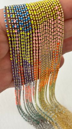 a hand holding several different colored bracelets in it's palm, with multiple rows of multicolored beads on each strand