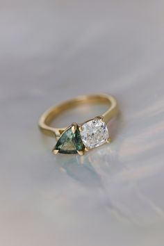 an engagement ring with two pear shaped green and white diamonds on it, set in yellow gold