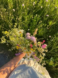 a person laying on the ground with flowers in their lap and hands behind them, surrounded by tall grass