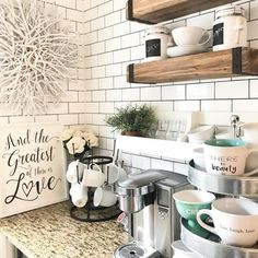 a kitchen counter with coffee cups and mugs on it, next to a sign that says and the greatest is love