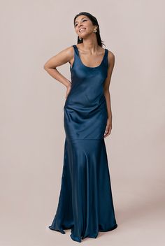 a woman in a long blue dress with her hands on her hips, looking to the side